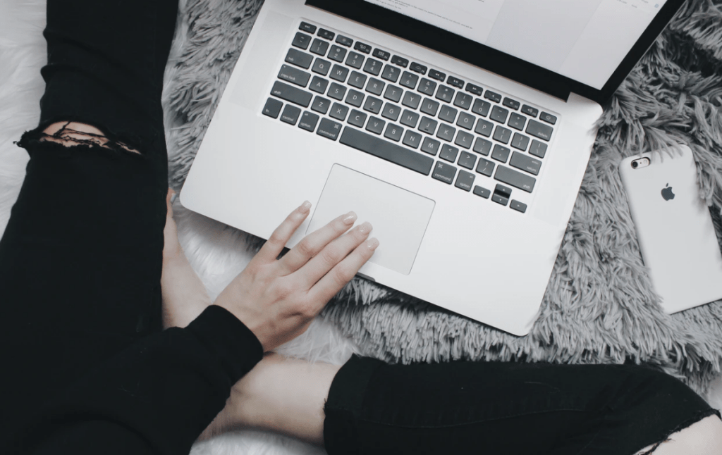 web content manager working on silver laptop, ripped black jeans