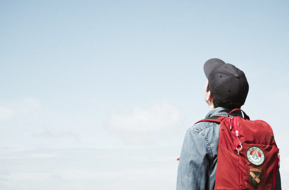 person standing with baseball hat and backpack, looking at the sky, scholarships and bursaries