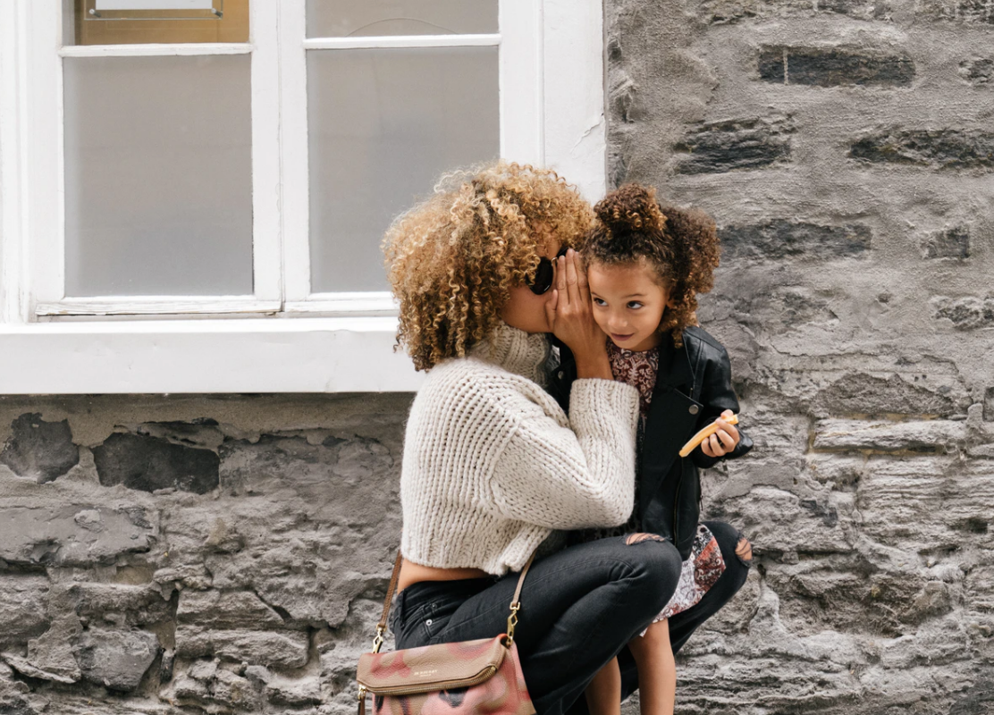 woman bending down to whisper to child for success in school