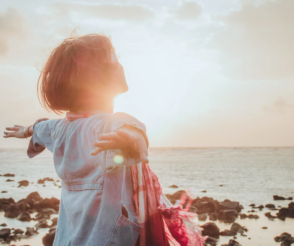 private schools , woman standing with arms out on beach during sunset